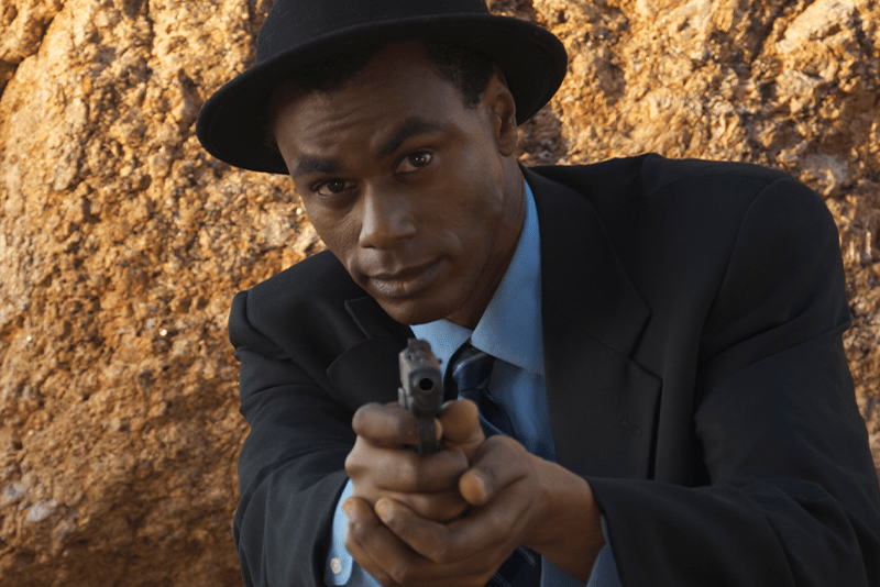 A black man in a hat holding a pistol